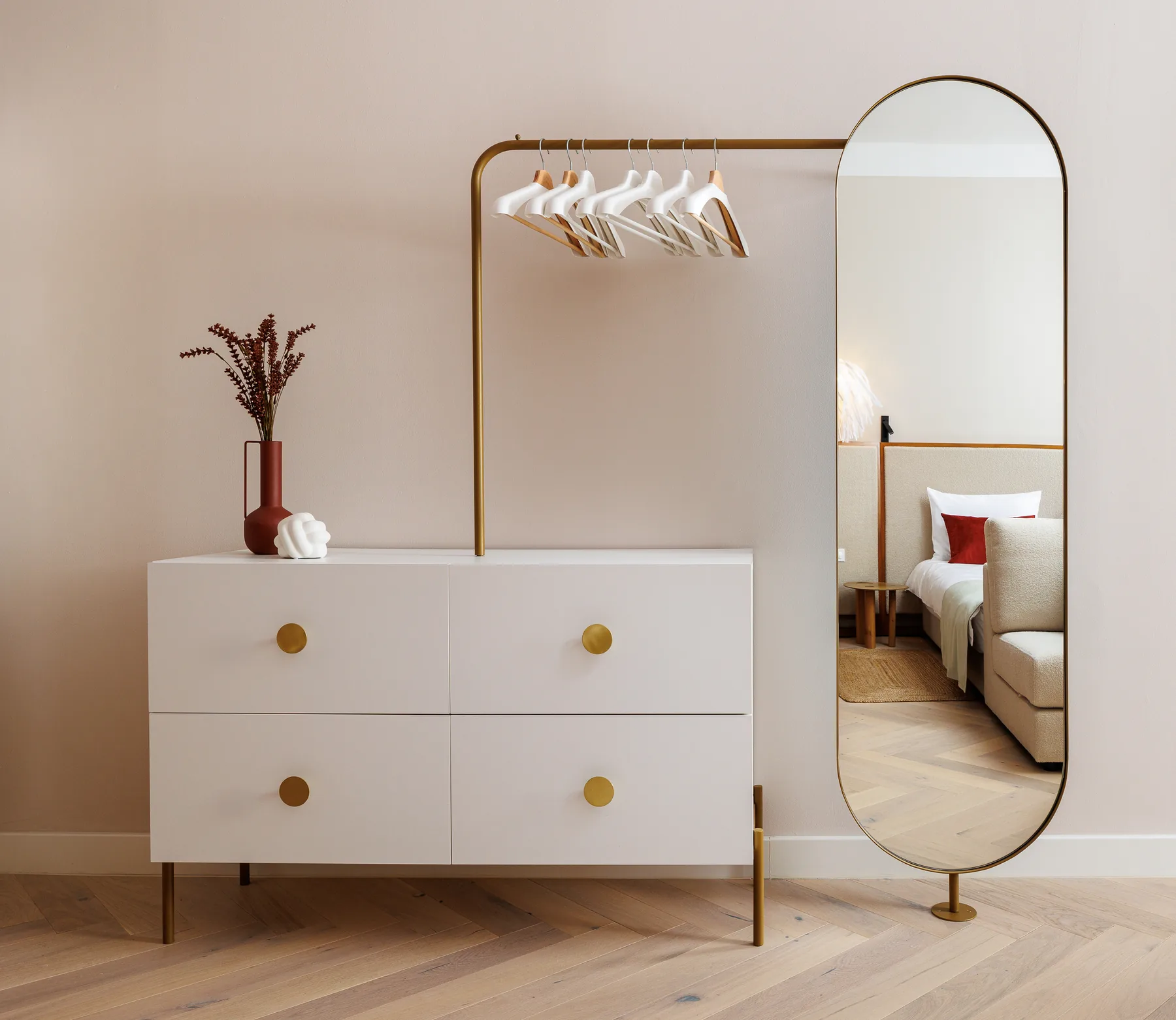 Pale drawers and a tall arched mirror in the dressing area