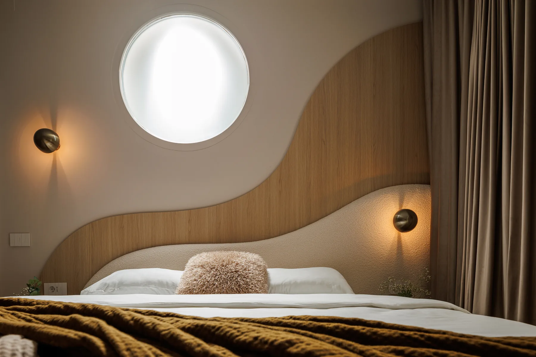 Curved timber headboard beneath a circular window at Roy Palace